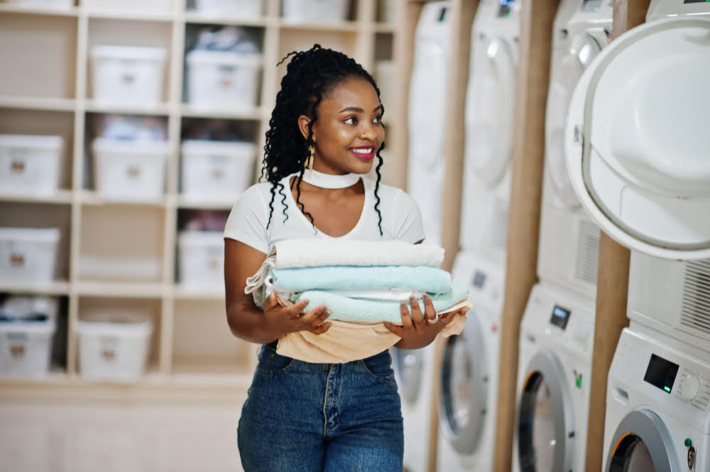 cheerful african american woman with towels hands near washing machine selfservice laundry